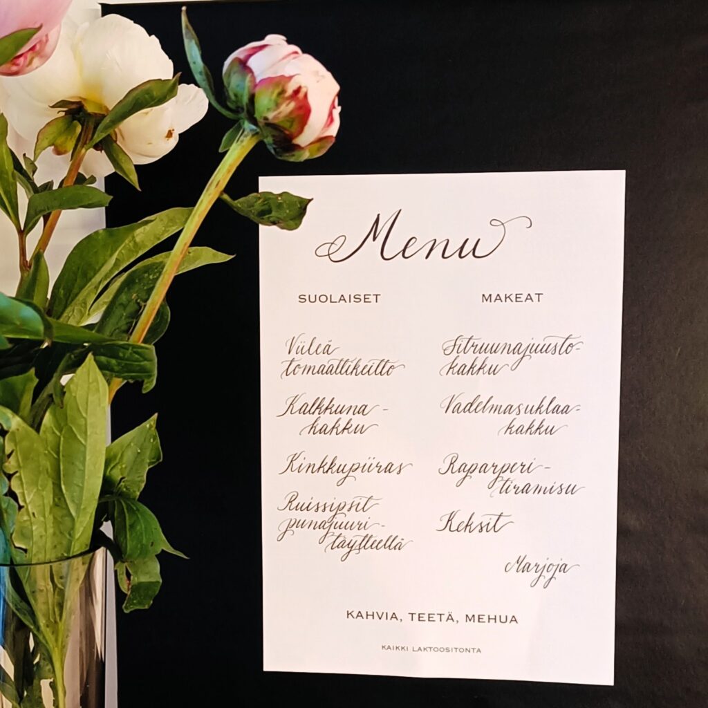 Menu jossa valkoisella pohjalla ruokalajit mustalla. Modernia kalligrafiaa.